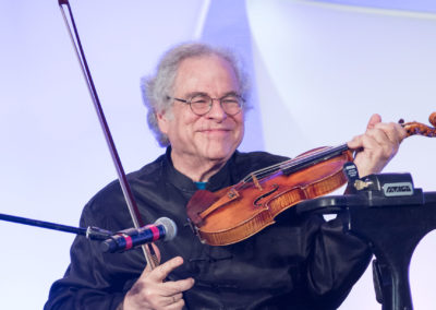 Violin virtuoso Itzhak Perlman holding violin and bow behind a microphone at the 2017 Bridges Gala