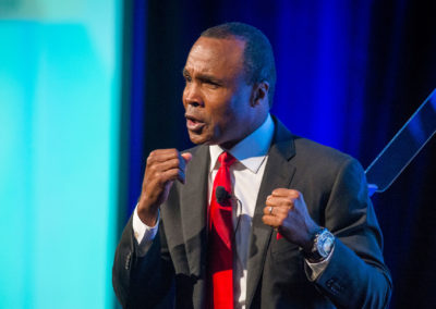 Olympic Gold Medalist and boxing legend Sugar Ray Leonard in a dark suit with red tie in a boxing stance at the 2016 Bridges Gala